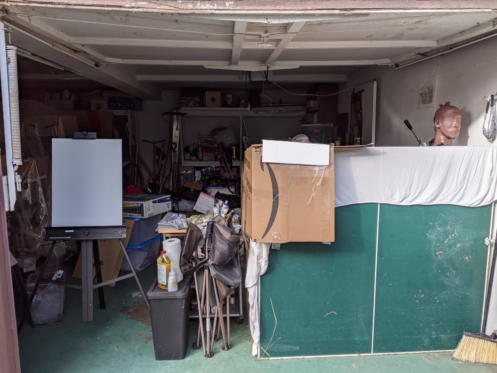A garage converted to a painting studio: an easel, cardboard boxes stacked to block daylight, a green ping-pong table